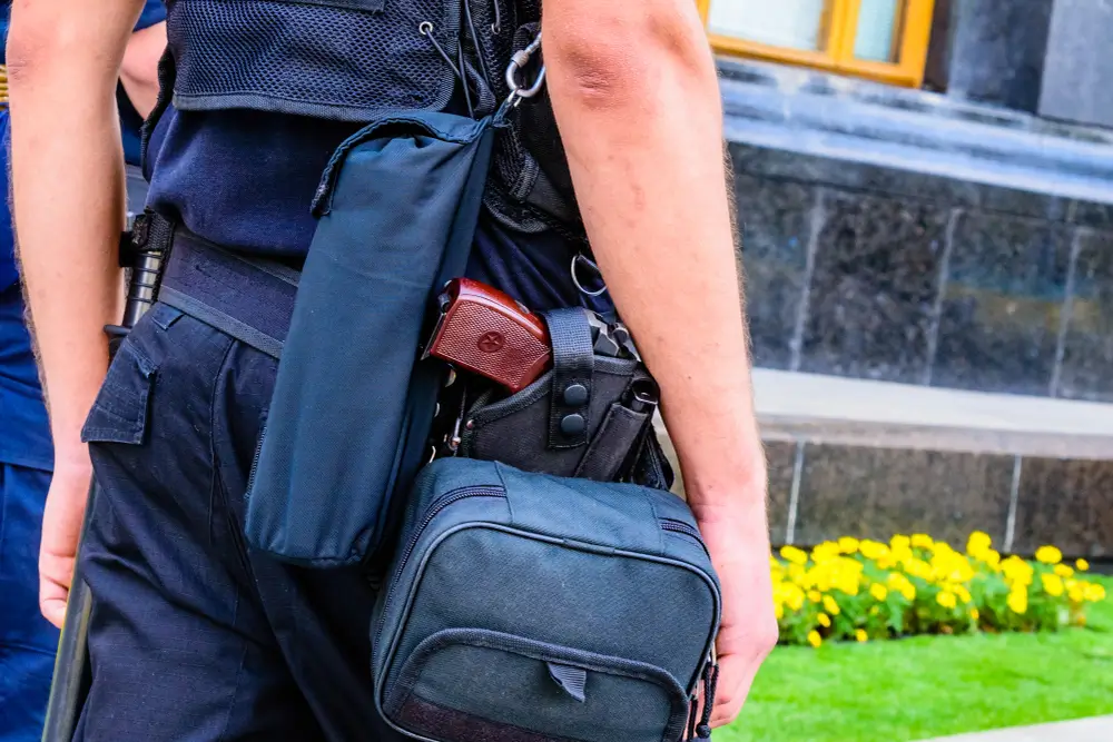 Cinturón policial con pistola reglamentaria y fundas de equipo táctico en el uniforme de un agente de seguridad en servicio.