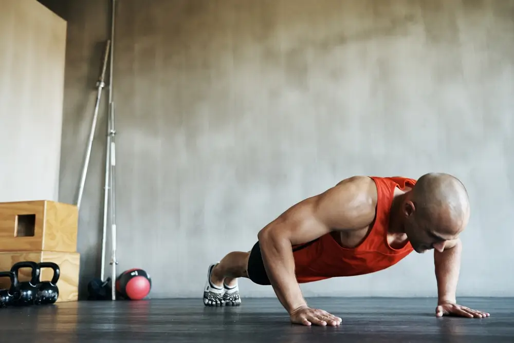 Hombre haciendo flexiones en un entrenamiento de gimnasio, manteniendo una técnica correcta para la prueba física.