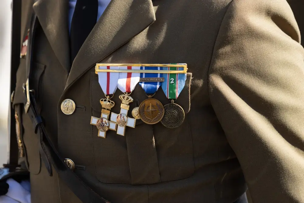 Condecoraciones y divisas sobre un uniforme militar, resaltando las medallas al mérito y los botones dorados de gala.