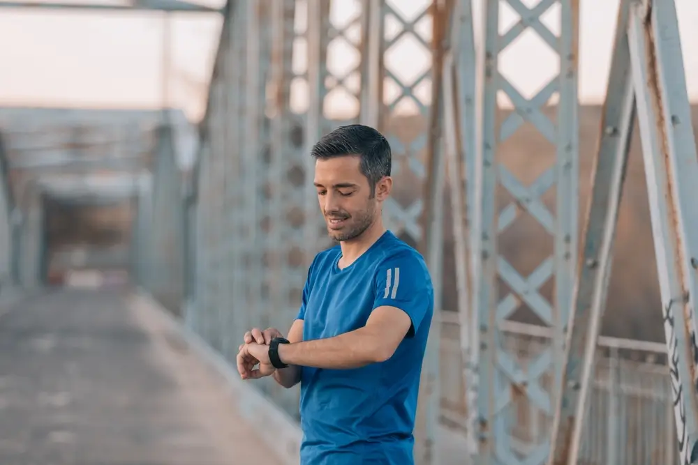 Atleta mirando su cronómetro en un puente para evaluar su progreso en el entrenamiento para la oposición.