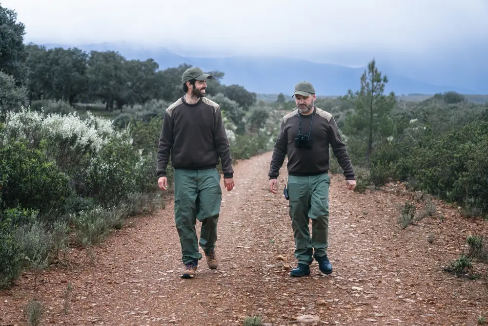 Dos agentes de una patrulla forestal recorren un sendero en un paisaje natural boscoso durante labores de vigilancia.