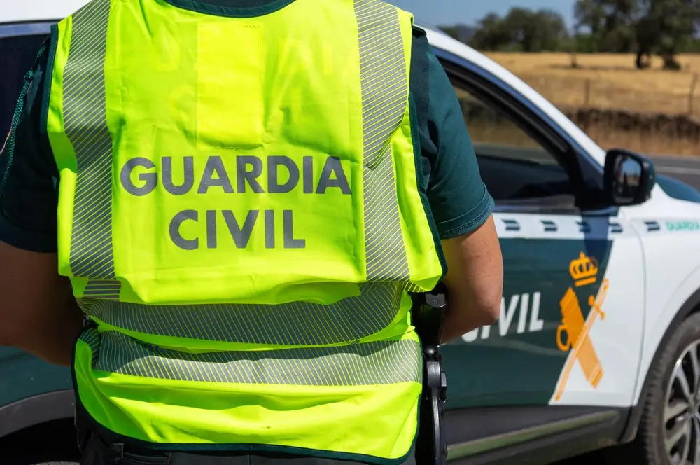 Agente de la Guardia Civil con chaleco reflectante patrullando junto a un vehículo oficial durante sus prácticas.