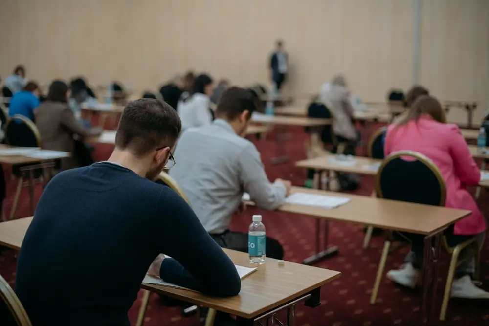 Aspirantes concentrados realizando un examen tipo test en pupitres individuales en un aula durante una oposición.