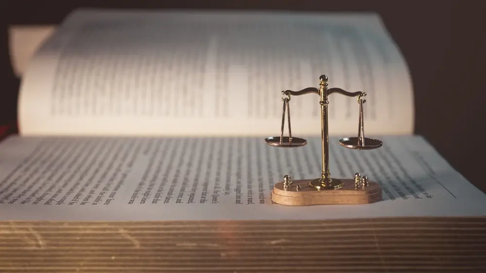 Balanza de la justicia sobre un libro abierto de leyes, representando los códigos legales y las bases del Derecho.