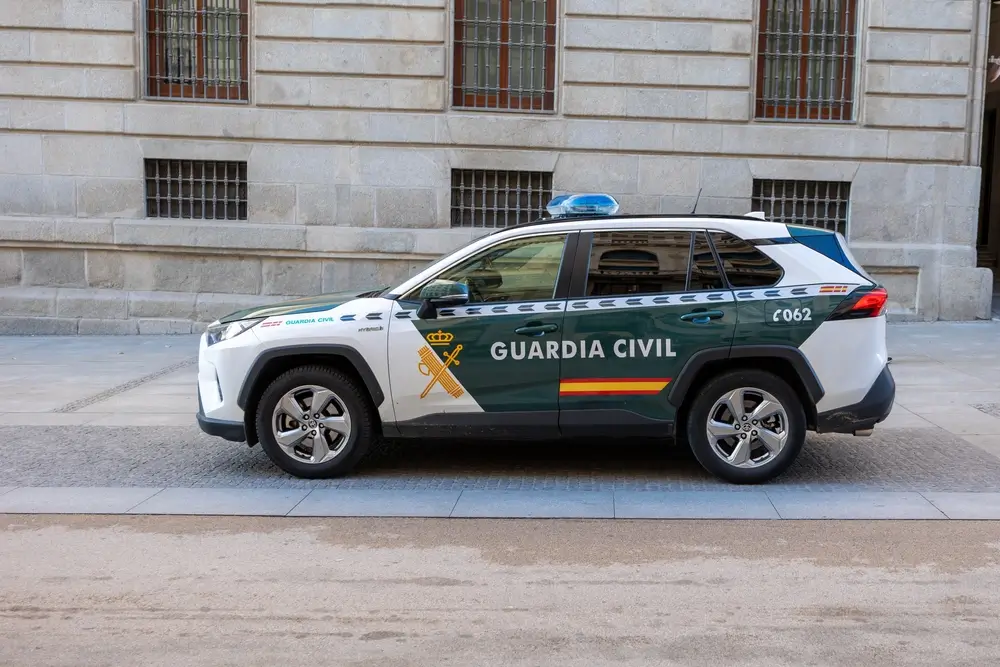Coche patrulla de la Guardia Civil blanco y verde estacionado en una calle española frente a un edificio de piedra.