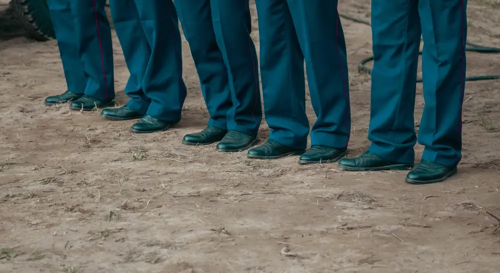 Pies de alumnos formados en el patio de armas de la academia militar, reflejando la disciplina de la instrucción.