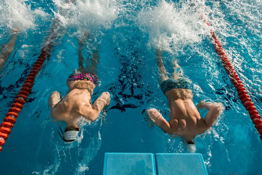Nadadores aproximándose a la pared para realizar un viraje en una piscina con corcheras rojas.