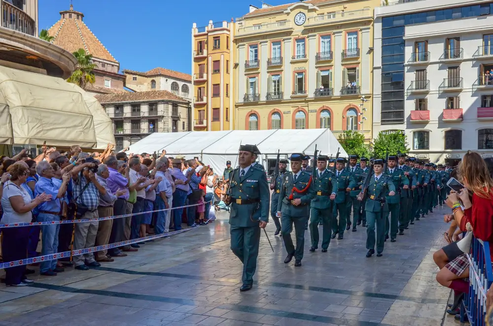 Agentes de la Guardia Civil marchando en formación con uniforme de gala durante un desfile oficial ante el público.
