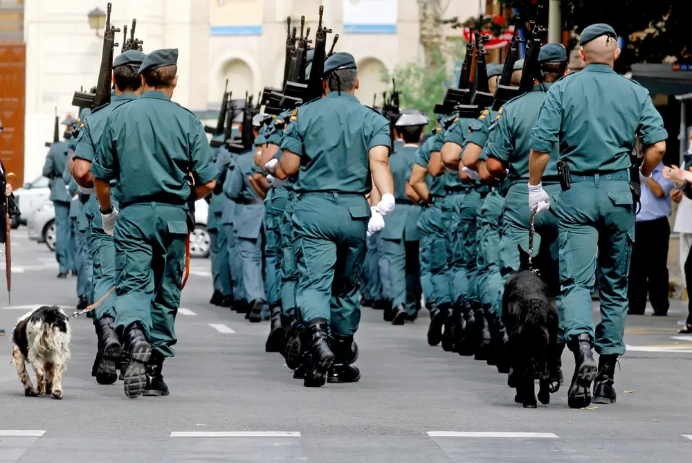 Agentes de la Guardia Civil marchando en formación con uniforme de servicio y fusiles en un acto oficial.