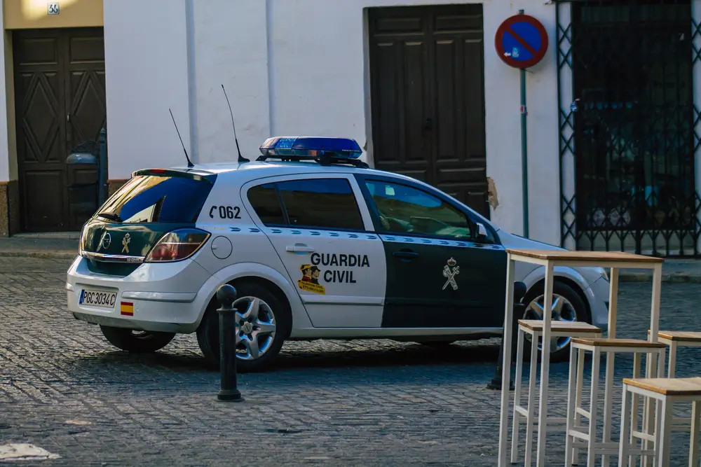 Coche patrulla de la Guardia Civil estacionado en una calle empedrada junto a una terraza y edificios blancos.