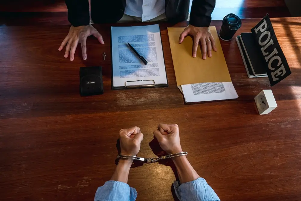 Agente de la Guardia Civil revisando documentos ante un detenido esposado durante una investigación policial.
