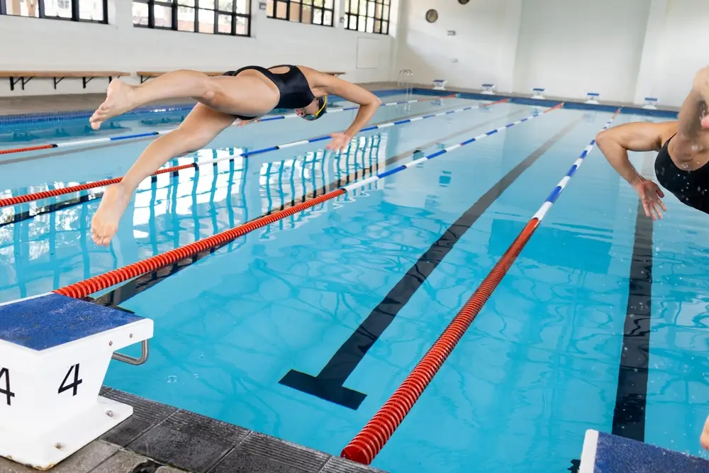 Nadadora saltando al agua desde el bloque de salida para entrenar en una piscina las pruebas de soltura acuática.