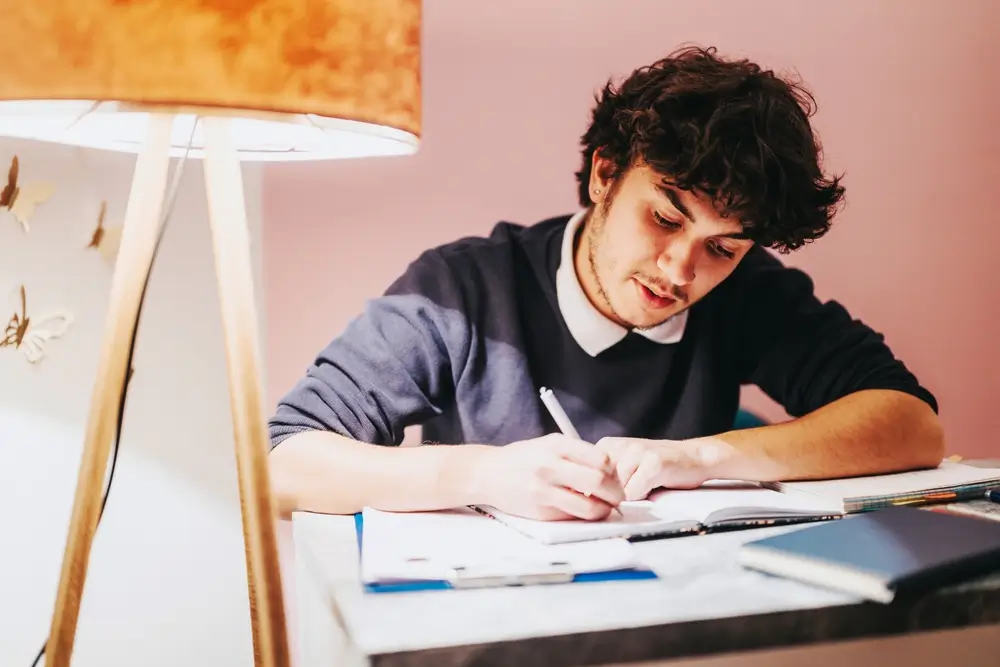 Joven opositor revisando material de estudio para oposiciones a la policía y tomando notas en su escritorio.