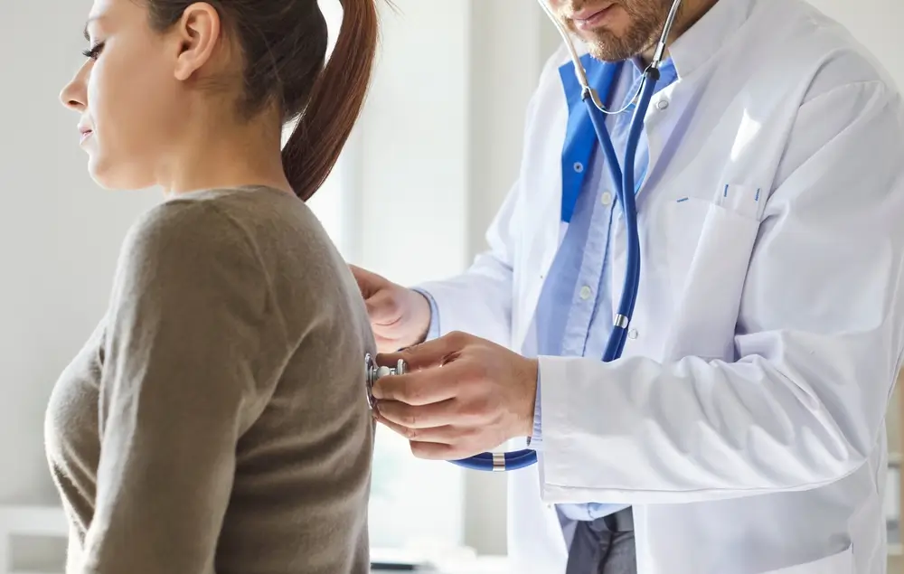 Médico auscultando la espalda de una aspirante con un estetoscopio durante un reconocimiento médico.