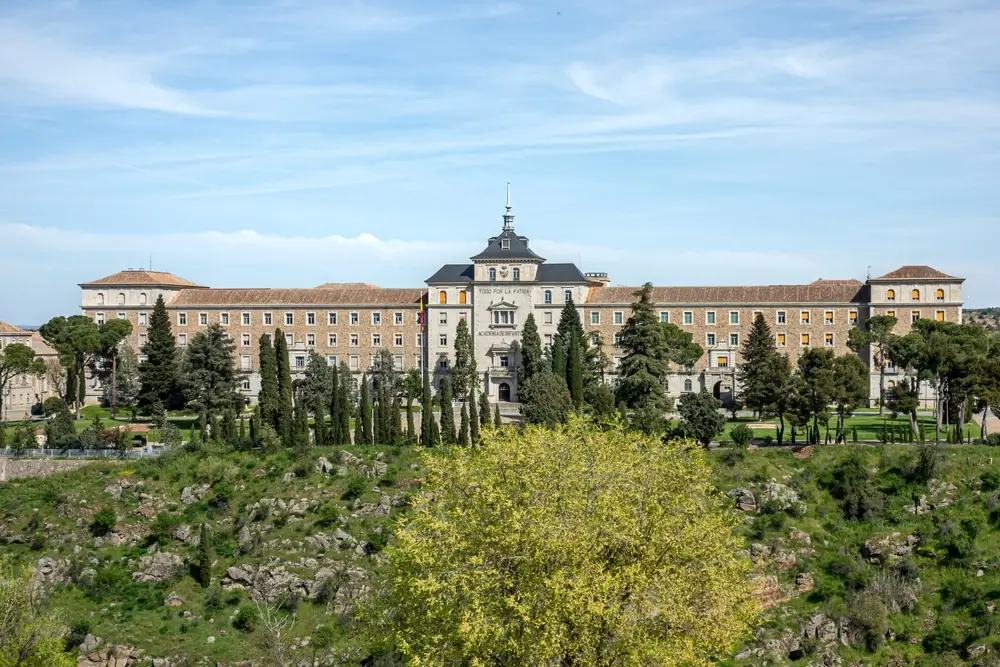 Fachada del cuartel y academia de la Guardia Civil, edificio histórico de piedra con torre central y jardines.