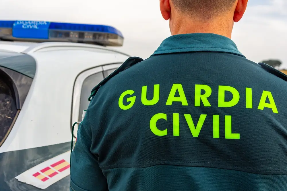 Agente de la Guardia Civil de espaldas luciendo el uniforme oficial junto a un vehículo patrulla.