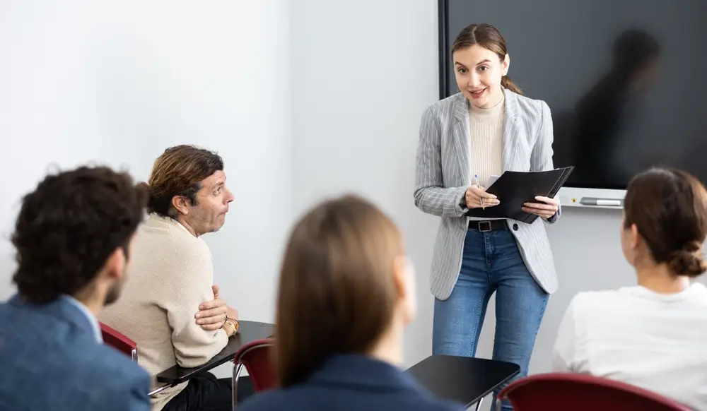 Profesora explicando la lección a alumnos sentados en el aula de una academia de preparación de oposiciones.