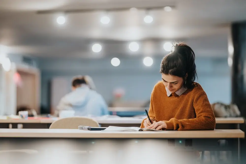 Estudiante concentrada preparando el examen de ortografía para las oposiciones de la Guardia Civil en una biblioteca.