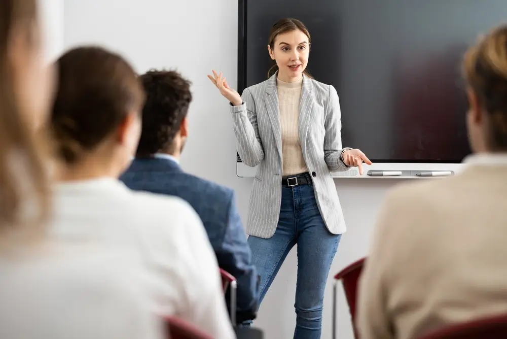 Profesora imparte formación a aspirantes en un aula de la academia frente a una pantalla digital.