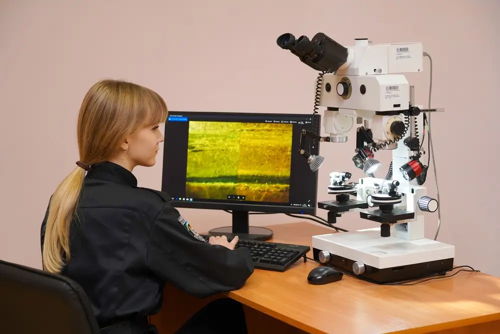 Agente policial utilizando equipo forense digital y microscopio para el análisis de pruebas en un laboratorio.