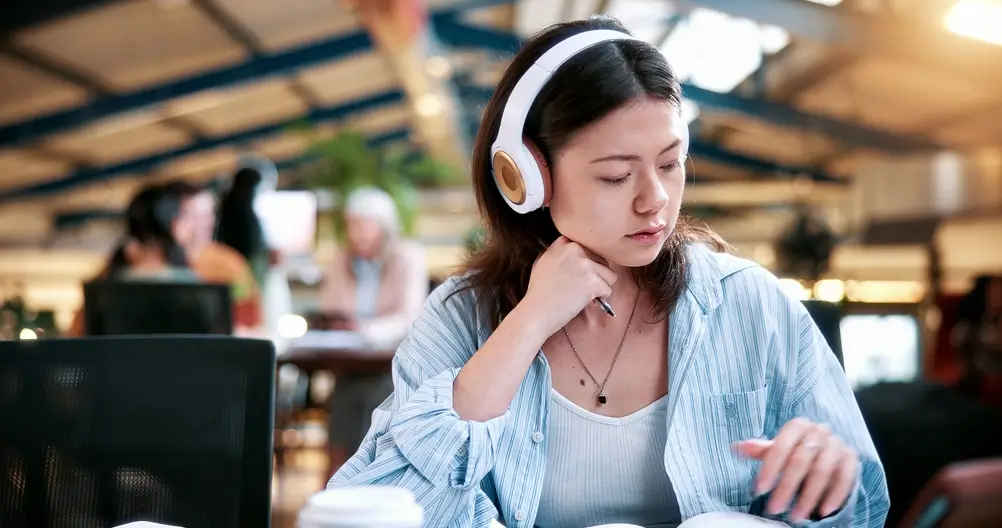 Mujer joven con auriculares estudiando idiomas en una biblioteca moderna para sumar puntos en sus méritos académicos.