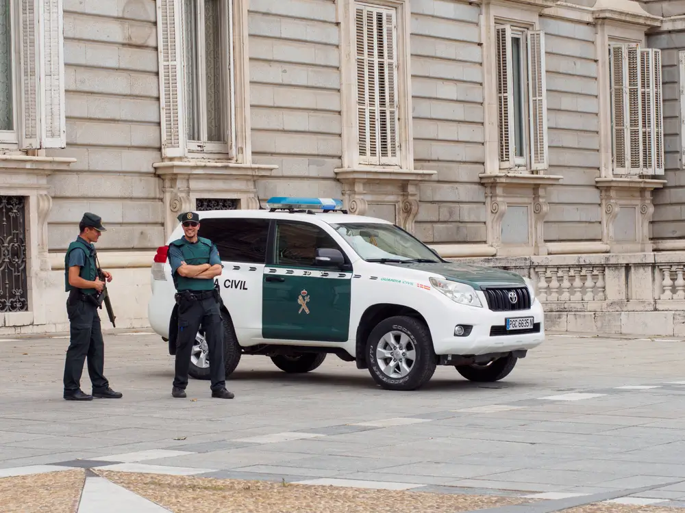 Agentes de la Guardia Civil junto a un coche oficial frente a la fachada de un cuartel o comisaría institucional.